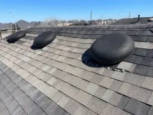 Two black plastic dome vents left in place on a roof the shingles were just replaced on